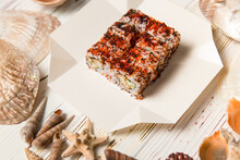 Japanese Sushi Roll On Carton Delivery Box. Sea Shells And Stars On Wooden Background. Asian Dish With Crunchy Tempura Shrimp, Cucumber, Rice And Colorful Flying Fish Roe (Tobiko Caviar).
