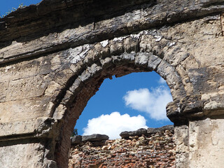 arched opening of a ruined ancient red brick building against a blue cloudy sky