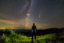 Dark Silhouette Of A Man Standing In Mountains At Night Enjoying Milky Way And Neowise Comet With Light Tail In Dark Sky View.