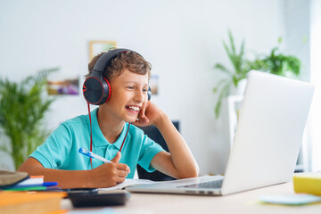 cheerful boy with headphones uses laptop to make a video call with his teacher.
