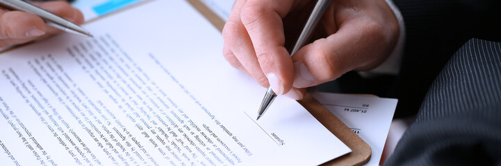 Male arm in suit and tie fill form clipped pad with silver pen closeup. Sign gesture read pact sale agent bank job make note loan credit mortgage investment finance executive chief legal teamwork law