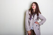 © papa - A beautiful fashionable woman in a light raincoat and a neckerchief poses on a light background.