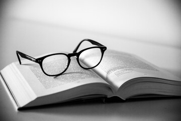 Wall Mural - Grayscale shot of a pair of glasses on an open book with a white background