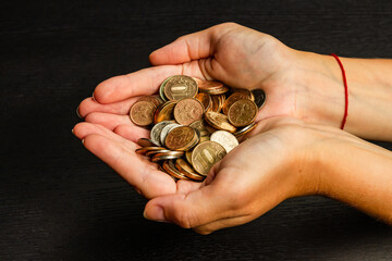 Wall Mural - girl holding a handful of coins in her hands on a black table background