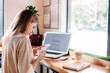 © Denis - Young girl with phone in hand works behind a laptop in a coffee shop and drinks a cappuccino