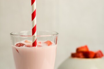 Canvas Print - Closeup shot of strawberry milkshake with straw and bowl of strawberries in the background