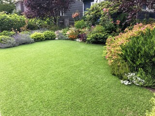 a beautiful artificial lawn in the front yard with nice flowers and shrubs surrounding it