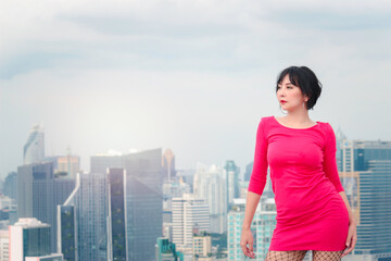 Portrait of cheerful confident young female standing with skyscraper city view. Attractive woman in red dress on rooftop