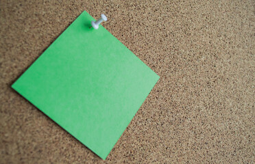  Close up of a green paper note on a cork Board, attached with a white pushpin. Copy space