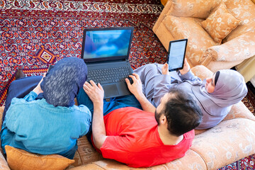 Wall Mural - Happy arabic family sitting on sofa and using technology