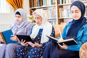 Wall Mural - Happy arabic muslim grandmother and grand daughter and mother sitting togther on couch using technology