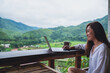 A beautiful asian woman working and typing on laptop computer while sitting on balcony with mountains and green nature background