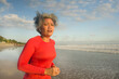 fit and attractive middle aged woman running on the beach - 40s or 50s mature lady with grey hair doing hard jogging workout enjoying fitness and healthy lifestyle