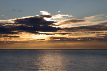 The seascape with dramatic clouds covering the sun and a smooth calm surface of the sea on background of a sunset.