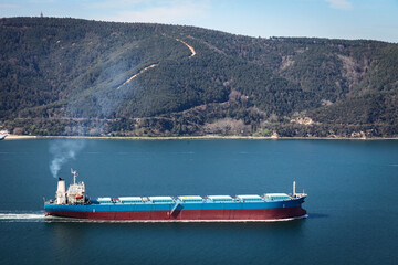 Huge cargo ship is passing through Istanbul strait or Bosporus. European side of Istanbul is visible. Aerial shot of a giant cargo ship with silos loaded.