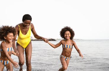 Wall Mural - Happy African family running on the beach during summer holidays - Afro American people having fun on vacation time - Parents love and travel lifestyle concept