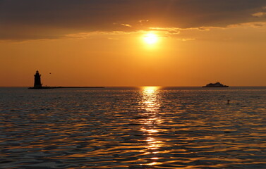 Wall Mural - A distance silhouette of the lighthouse and a boat during sunset at Cape Henlopen State Park, Lewes, Delaware, U.S.A