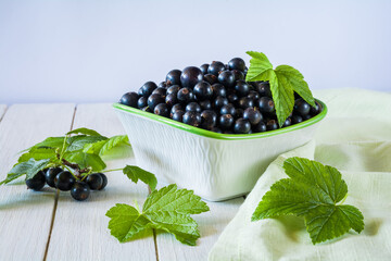 Wall Mural - Ripe black currant berries in a bowl on a white wooden table