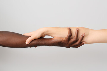 Wall Mural - Caucasian woman and African-American man holding hands together on light background. Racism concept