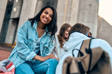 Wall Mural - Attractive African American girl student sits on the steps near the campus with her friends.