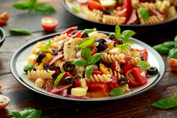 Antipasto salad with pasta, tomato, olives, red onion, bell pepper, salami, cheese, artichoke and basil.