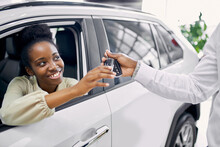 Portrait Of Good-looking Afro Lady Getting Keys By Car, Woman Make Purchase In Cars Showroom. She Sits Inside Of Beautiful Car And Look At Sales Agent