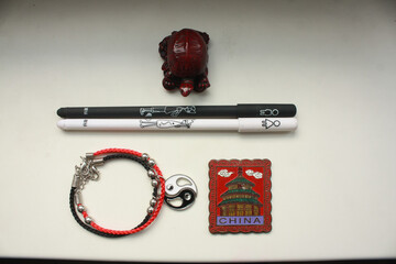 A composition of a Chinese red tortoise figurine, a black and white pen, a bracelet with a yin yang symbol and a metal magnet with a Chinese building on a white background.