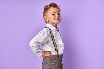 portrait of beautiful caucasian little child boy posing at camera isolated over purple background, kid looks at camera and smile