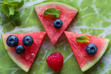 Slices of watermelon covered with red fruit and mint.