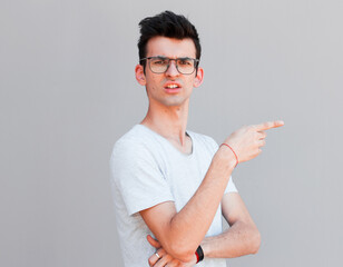 Wall Mural - Handsome man in casual clothes is pointing away, looking at camera and smiling, on gray background