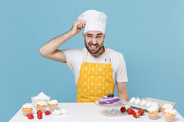 Wall Mural - Preoccupied young bearded male chef or cook baker man in apron white t-shirt toque chefs hat cooking at table isolated on blue background. Cooking food concept. Mock up copy space. Put hand on head.