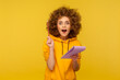 © khosrork - Portrait of inspired joyful curly-haired woman in urban style hoodie looking amazed with sudden genius idea and holding pencil to write in notebook. indoor studio shot isolated on yellow background