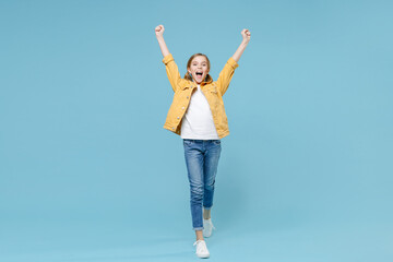 Canvas Print - Full length portrait of excited little blonde kid girl 12-13 years old in yellow jacket isolated on blue wall background. Childhood lifestyle concept. Mock up copy space. Clenching fists like winner.