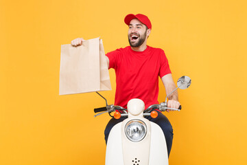 Delivery man in red cap t-shirt uniform driving moped motorbike scooter hold craft paper packet with food isolated on yellow background studio Guy employee working courier Service quarantine concept