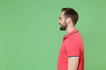 Side view of smiling young bearded man guy in casual red pink t-shirt posing isolated on green background studio portrait. People sincere emotions lifestyle concept. Mock up copy space. Looking aside.