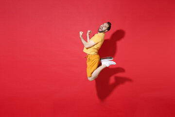 Sticker - Side view of screaming young bearded man guy in casual yellow t-shirt posing isolated on red background studio portrait. People lifestyle concept. Mock up copy space. Jumping doing winner gesture.