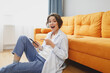 © ViDi Studio - Shocked young woman girl in white casual clothes sit on floor near couch spending time in living room at home. Rest relax good mood leisure lifestyle concept. Pointing index finger on mobile phone.