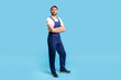 © khosrork - Full length confident professional handyman in overalls standing with crossed hands, smiling at camera. Profession of service industry, house repair. indoor studio shot isolated on blue background