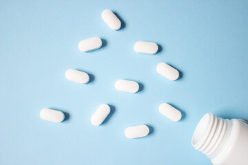 Wall Mural - White pills and white medical bottle on a blue background top view.