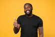 © ViDi Studio - Smiling african american man guy football fan in casual black t-shirt isolated on yellow background studio portrait. People sincere emotions lifestyle concept. Mock up copy space. Showing thumb up.