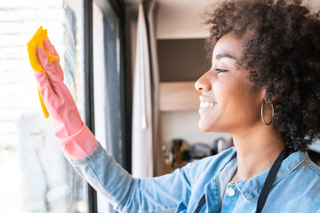 Wall Mural - Afro woman cleaning window with rag at home.