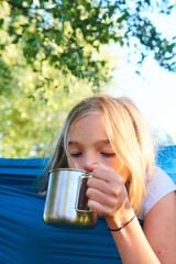 Wall Mural - Child girl lying in a hammock and drinking water from a tin cup