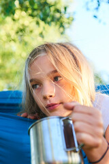 Wall Mural - Child girl lying in a hammock and drinking water from a tin cup