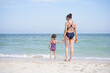 © Andrii - Mother daughter beach together rear view Unrecognizable caucasian woman little girl swimwear standing seaside back.