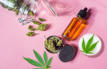 Medical Marijuana Jar flower buds CBD lotion, Oil and weed Grinder on pink background