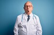 Senior grey haired doctor man wearing stethoscope and medical coat over blue background afraid and shocked with surprise expression, fear and excited face.
