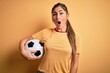 © Krakenimages.com - Beautiful brunette player woman playing soccer using football ball over yellow background scared in shock with a surprise face, afraid and excited with fear expression