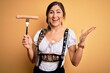 © Krakenimages.com - Young brunette german woman wearing traditional Octoberfest dress holding sausage very happy and excited, winner expression celebrating victory screaming with big smile and raised hands
