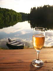 Wall Mural - Close-up on a glass of wine on a table with a lake and a boat in background