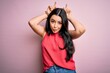 © Krakenimages.com - Young brunette woman wearing casual summer shirt over pink isolated background doing funny gesture with finger over head as bull horns